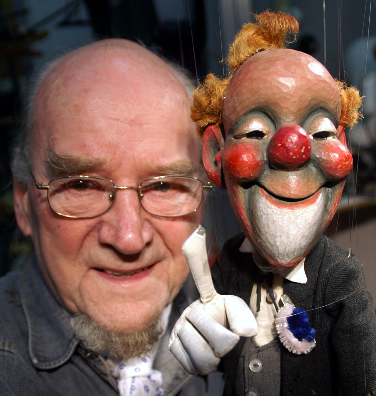Ein älterer Mann posiert mit einer Marionette, die einen fröhlichen Clown darstellt, in einem kreativen Atelier.