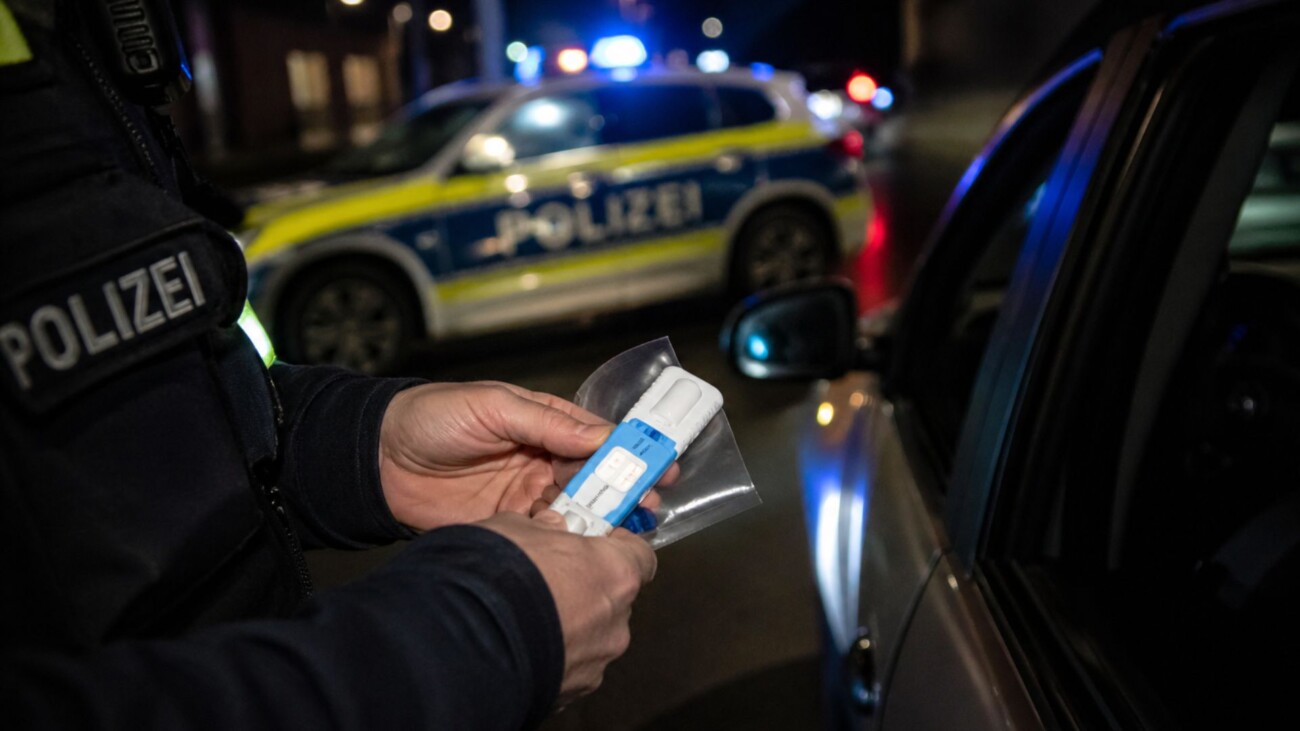 Ein Polizeibeamter hält einen Alkoholtest in der Hand, während ein Polizeiauto im Hintergrund steht.