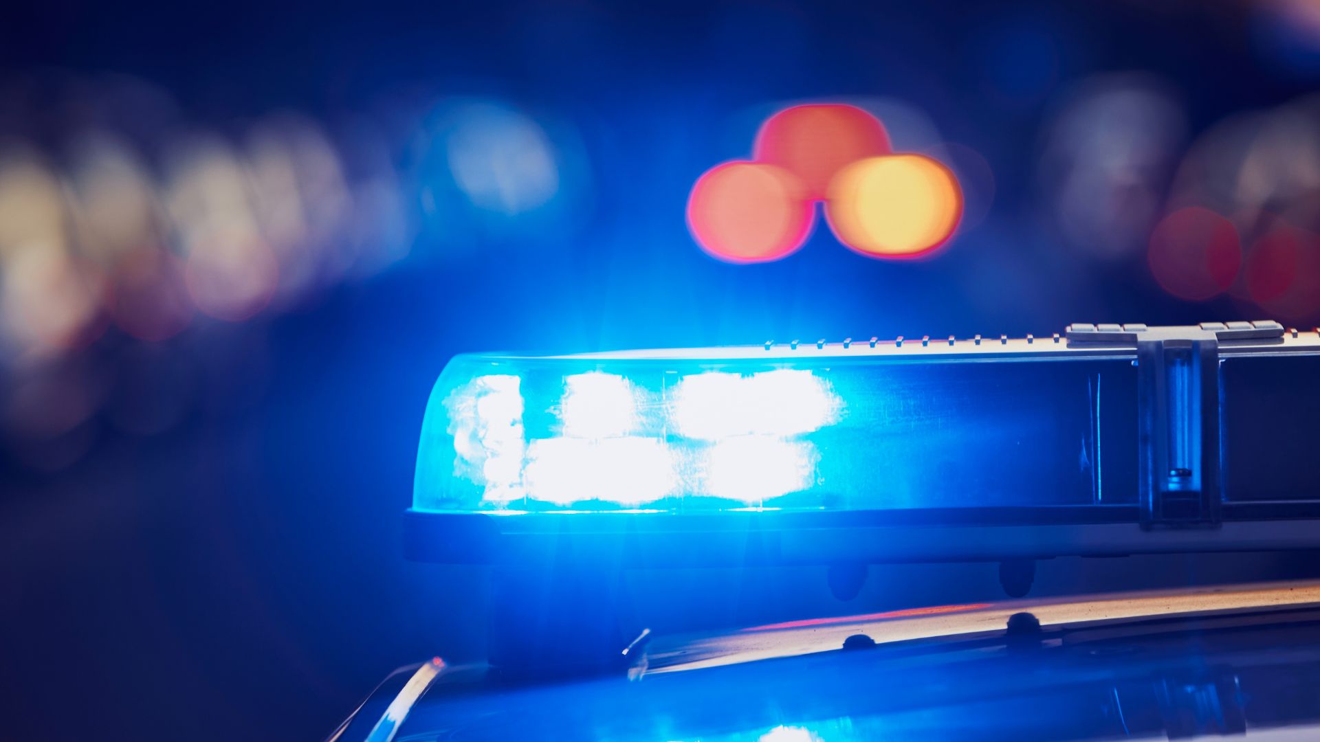 Nahaufnahme eines Polizeiautos mit eingeschaltetem Blaulicht bei Nacht, Hintergrund unscharf.