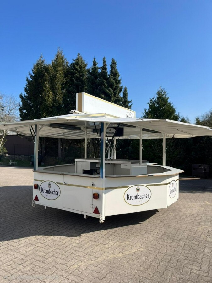 Ein Krombacher Verkaufsstand steht auf einem gepflasterten Platz unter blauem Himmel.