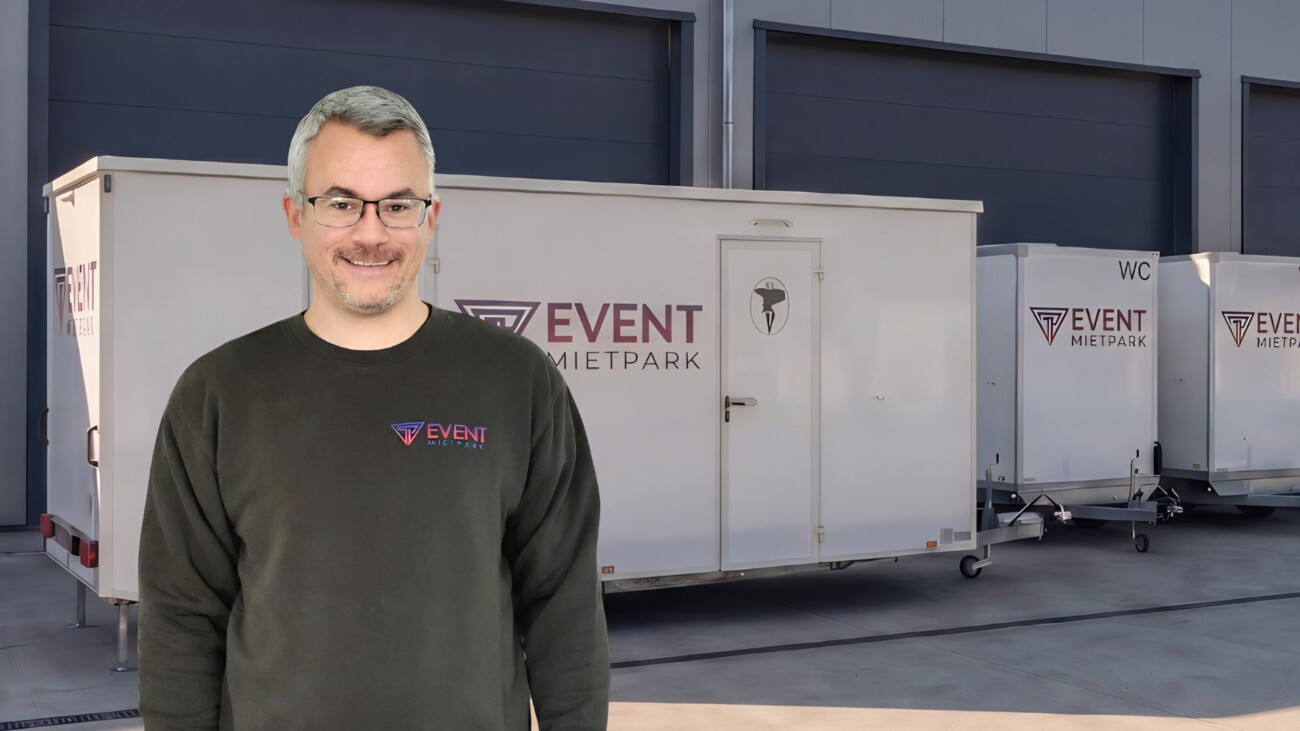 Ein Mitarbeiter von Pfannebecker Eventservice steht vor mobilen Toilettenanhängern in einer modernen Lagerhalle.