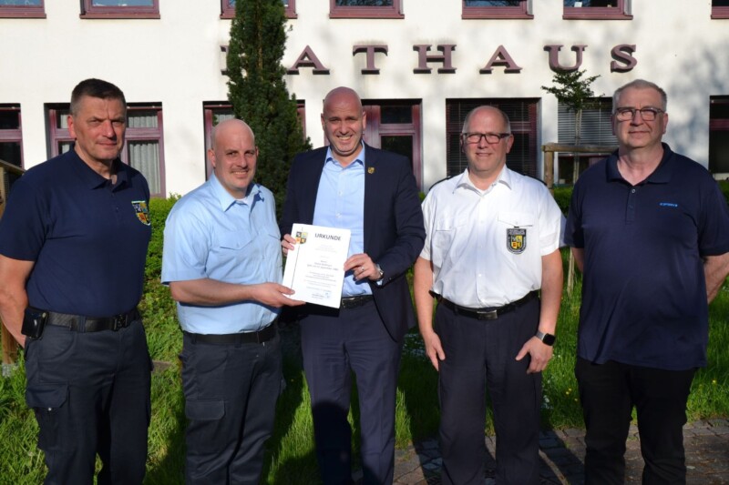 Fünf Männer stehen vor dem Rathaus und halten eine Urkunde in der Hand. Sie wirken stolz und zufrieden.