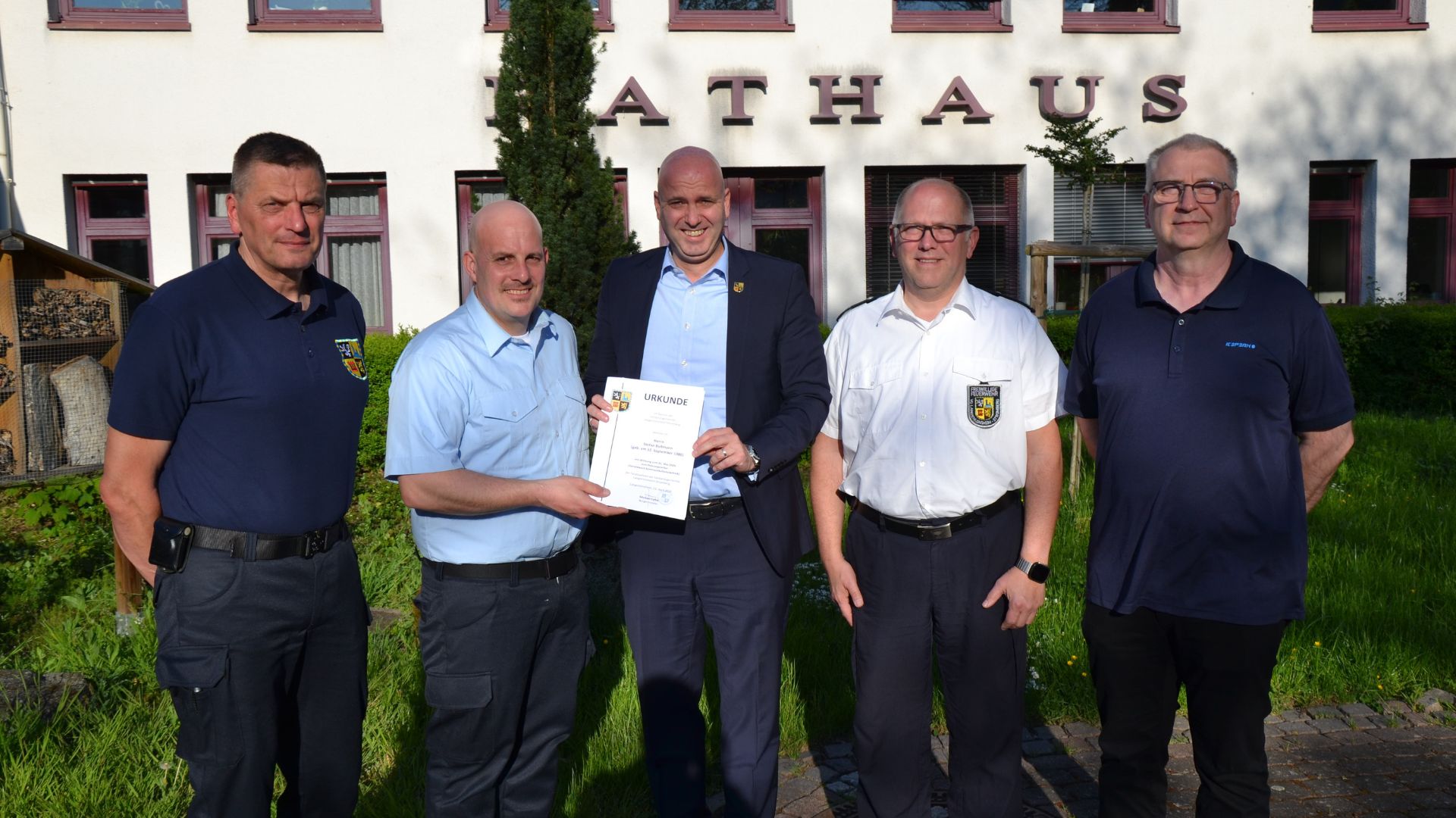 Fünf Männer stehen vor dem Rathaus und halten eine Urkunde in der Hand. Sie wirken stolz und zufrieden.