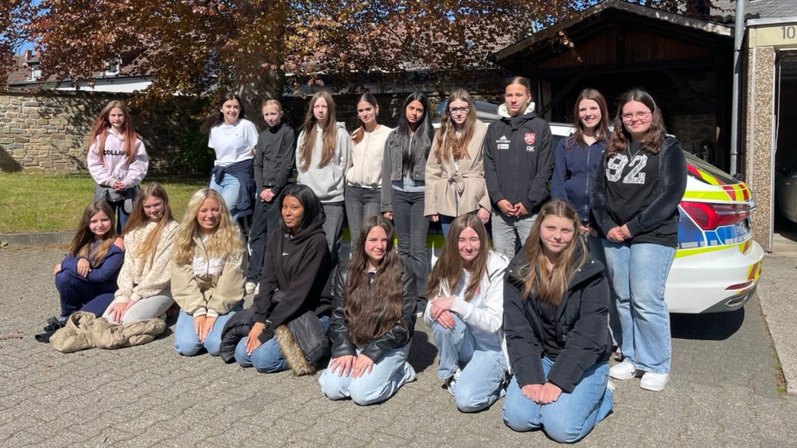 Gruppe von Jugendlichen posiert vor einem Polizeiauto an einem sonnigen Tag im Freien.