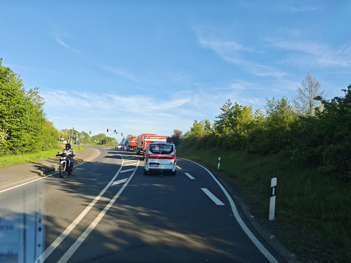 Ein Motorradfahrer und mehrere Fahrzeuge auf einer kurvenreichen Straße unter blauem Himmel und grüner Vegetation.
