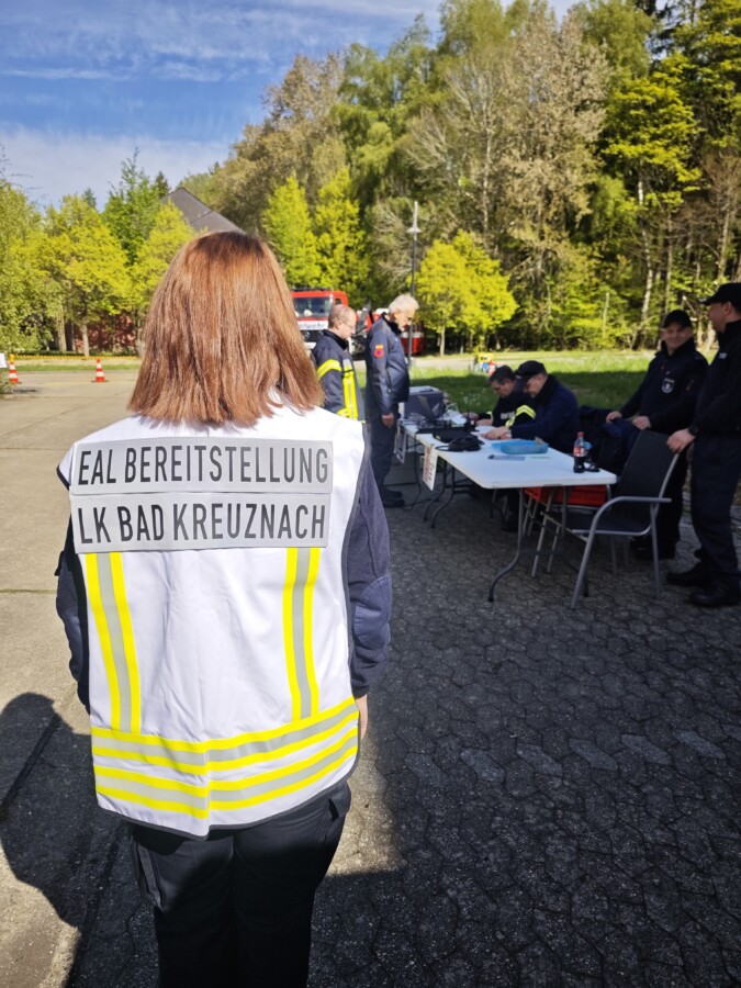 Eine Person in einer Warnweste mit der Aufschrift LK Bad Kreuznach steht vor einem Einsatzteam im Freien.