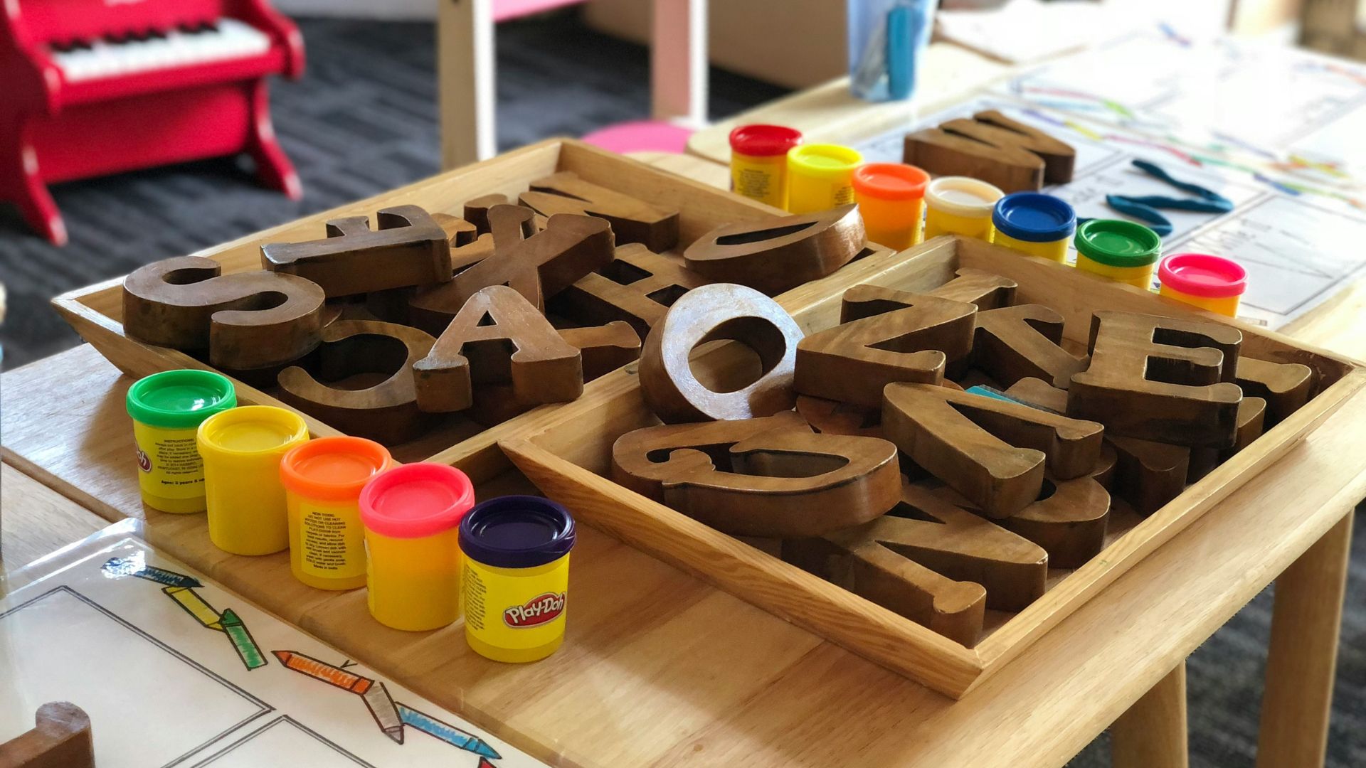 Holzbuchstaben und bunte Knetmasse auf einem Tisch in einem Lernraum für Kinder.