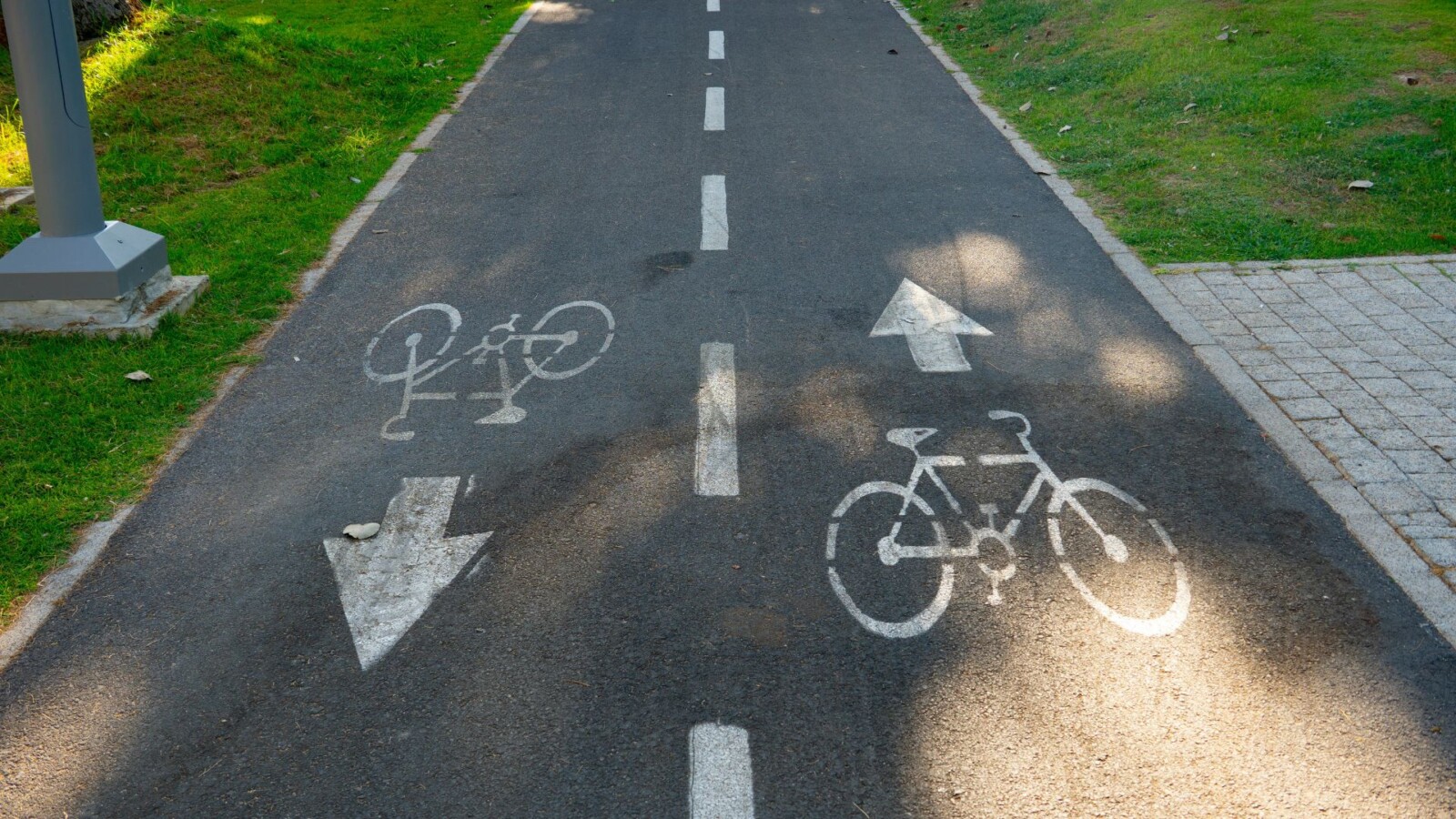 Fahrradweg mit Richtungspfeilen und Fahrrad-Symbolen auf asphaltierter Fläche.