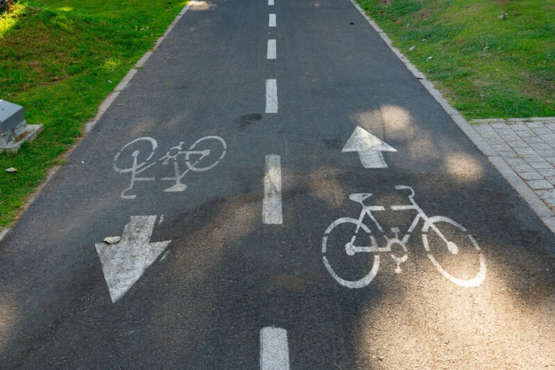 Fahrradweg mit Richtungspfeilen und Fahrrad-Symbolen auf asphaltierter Fläche.