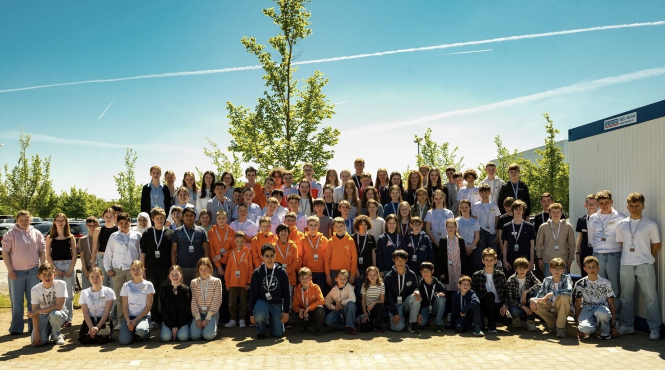 Gruppenfoto von Schülern und Lehrern im Freien, umgeben von Bäumen und einem blauen Himmel.