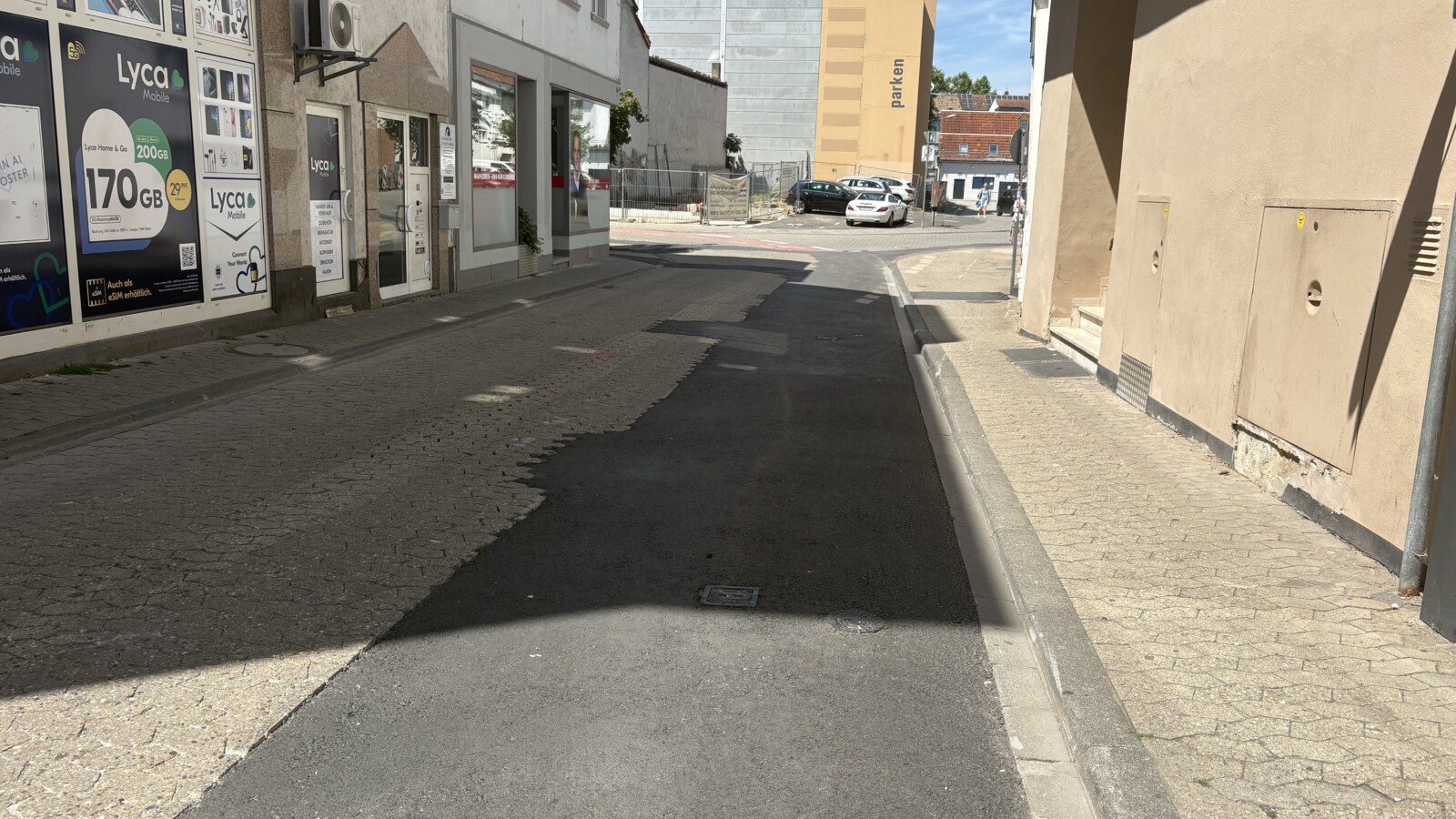 Straße nach Baumaßnahmen der Kreuznacher Stadtwerke mit neu asphaltiertem Abschnitt zwischen noch vorhandenen Pflasterflächen in einer Innenstadt.