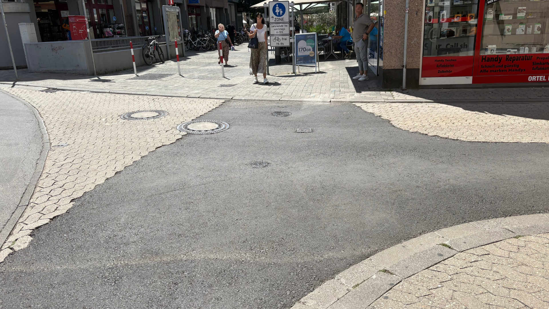 Straße nach Baumaßnahmen der Kreuznacher Stadtwerke mit neu asphaltiertem Abschnitt zwischen noch vorhandenen Pflasterflächen in einer Innenstadt.