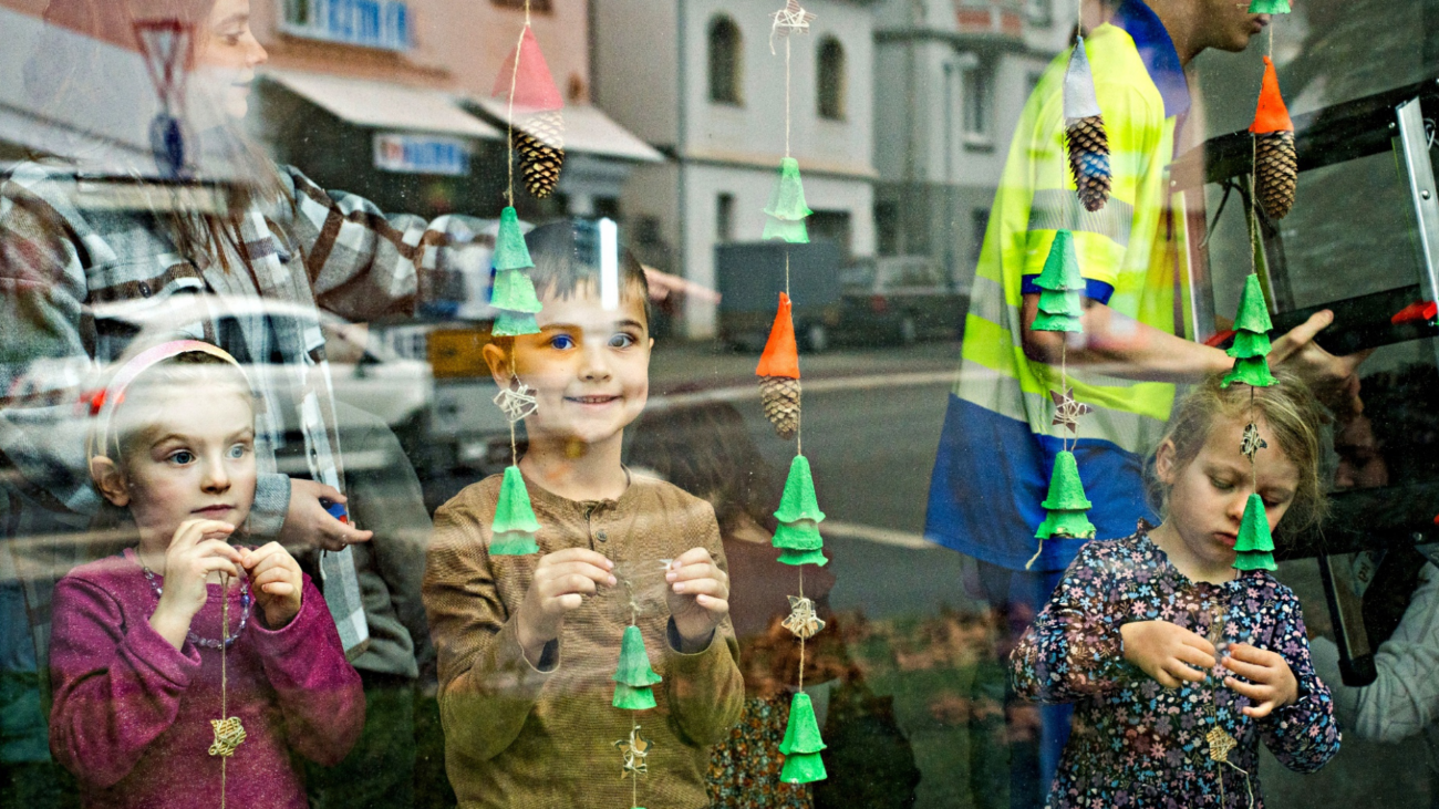 Die Kinder der beidenGewinner-Kindergärtenpräsentieren stolz ihren selbstgebastelten Fensterschmuck vor dem OIEVerwaltungsgebäude –gemeinsam mit Florian Schmidt, Kommunalbetreuer der OIE, und Thomas Johann, Vorstand der OIE.